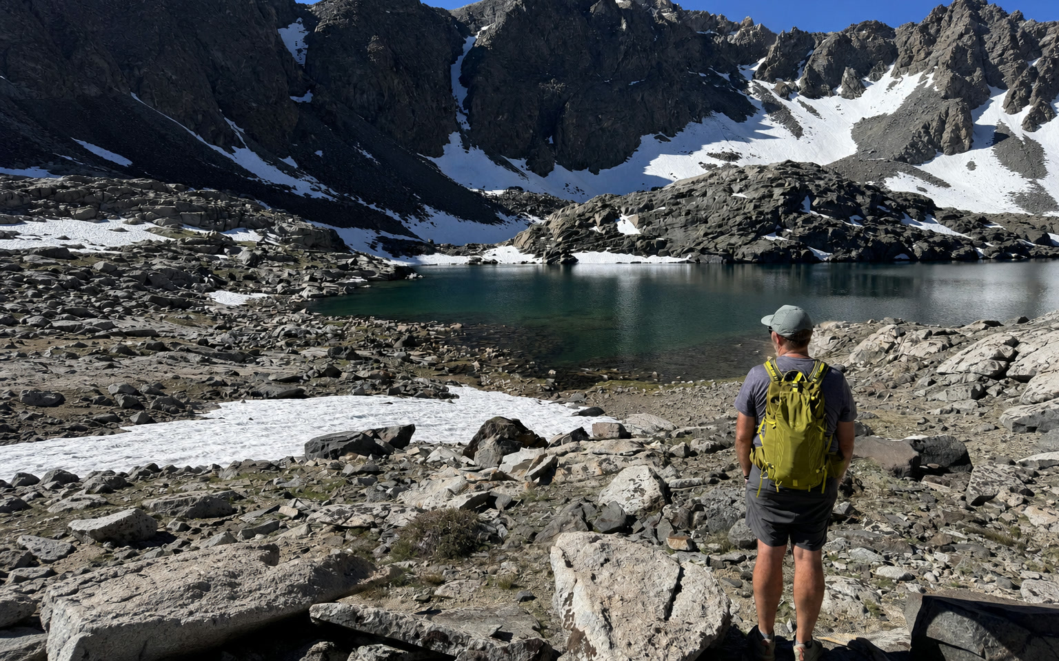 David overlooking a rocky alpine lake beneath a snow-lined mountain ridge